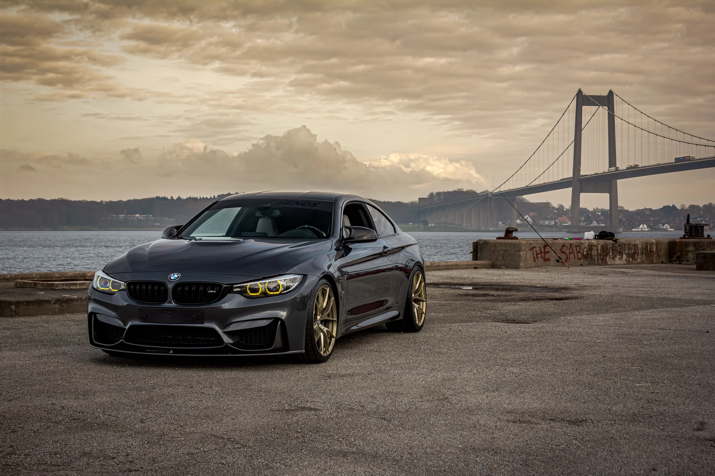 Mineralgrå BMW M4 på guldfælge foran Lillebæltsbroen ved solnedgang